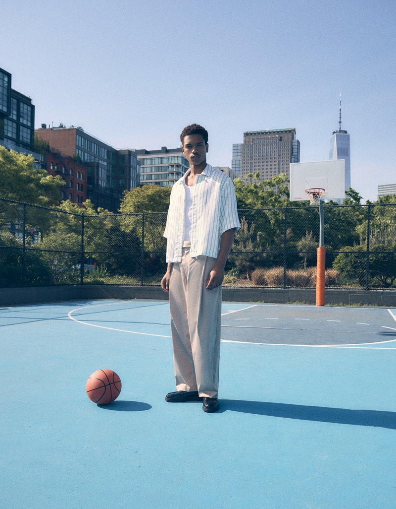 Bershka Summer 2024 004 Nile Winchester poses on a basketball court in relaxed trousers and a striped short-sleeve shirt.