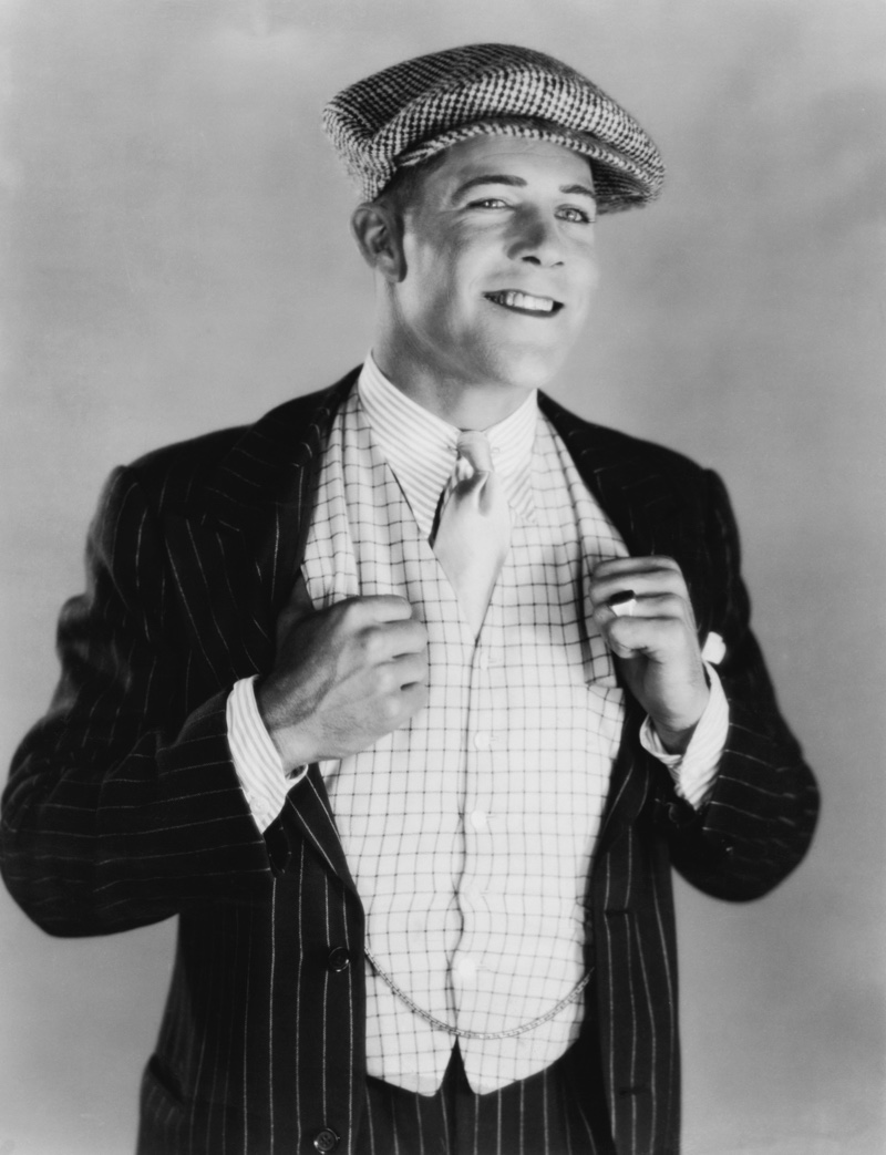 Mens Three Piece Suit 1920s Actor Kenneth Harlan wears a stylish vest with a pinstripe suit, a striped shirt, and a collar pin along with a flat cap.