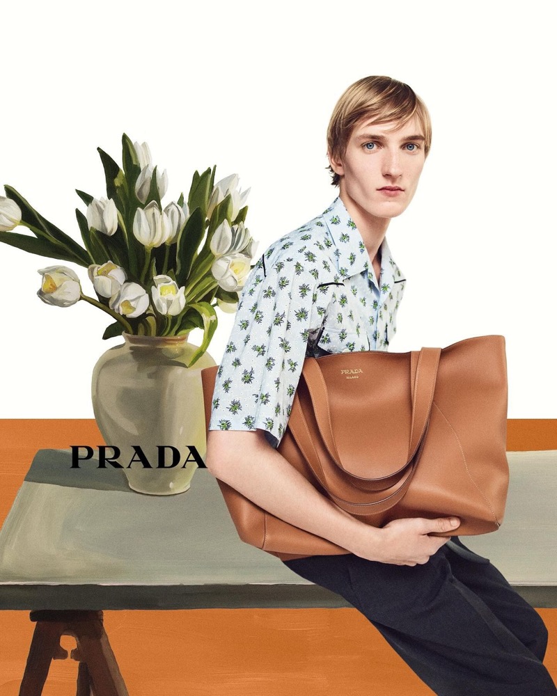 Prada Summer 2024 Campaign 005 Posing with a leather tote bag, Pierrick Grégoire wears a printed short-sleeve shirt for Prada's summer 2024 campaign.